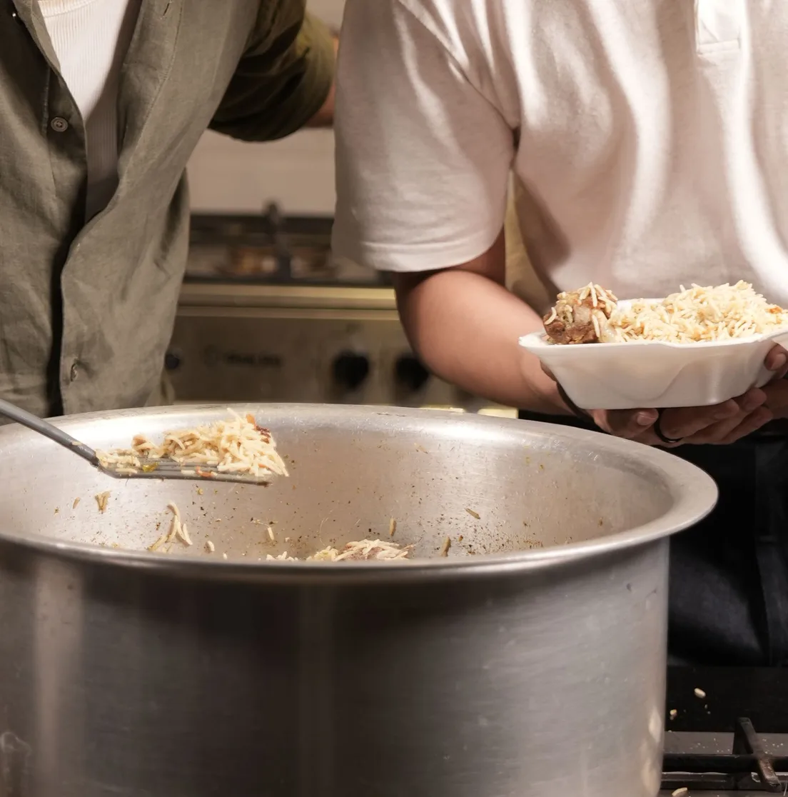 Freshly cooked rice being plated from the pot into a dawat box